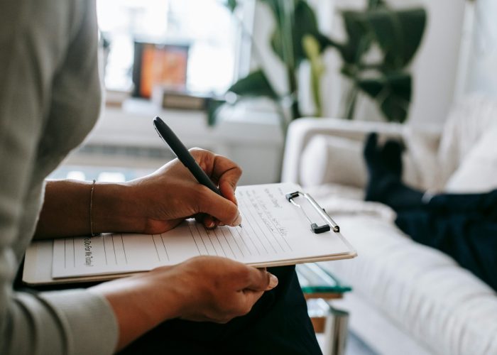 pexels-photo-5699456-5699456 Unrecognizable ethnic female therapist taking notes on clipboard while filling out form during psychological appointment with anonymous client lying on blurred background